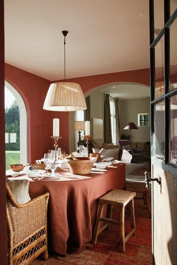 Gedeckter Esstisch mit lachsrotem Tischtuch passend zur Wandfarbe und Blick durch breiten Rundbogen ins Wohnzimmer