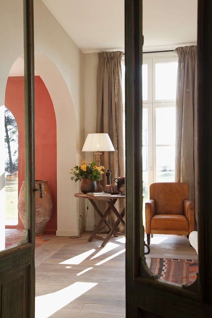Blick durch offene Tür mit Glasfüllung in schlichtes Wohnzimmer mit gemütlichem Platz vor Fenster