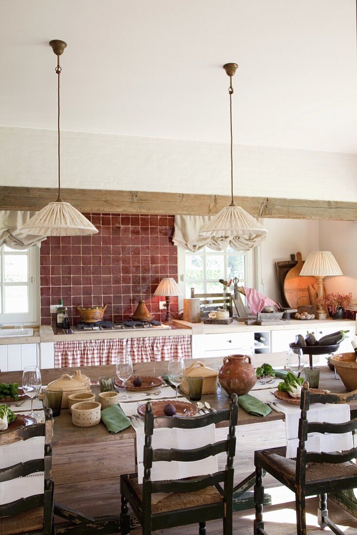 Vintage pendant lamps with fabric lampshades above set table and antique wooden chairs in rustic kitchen