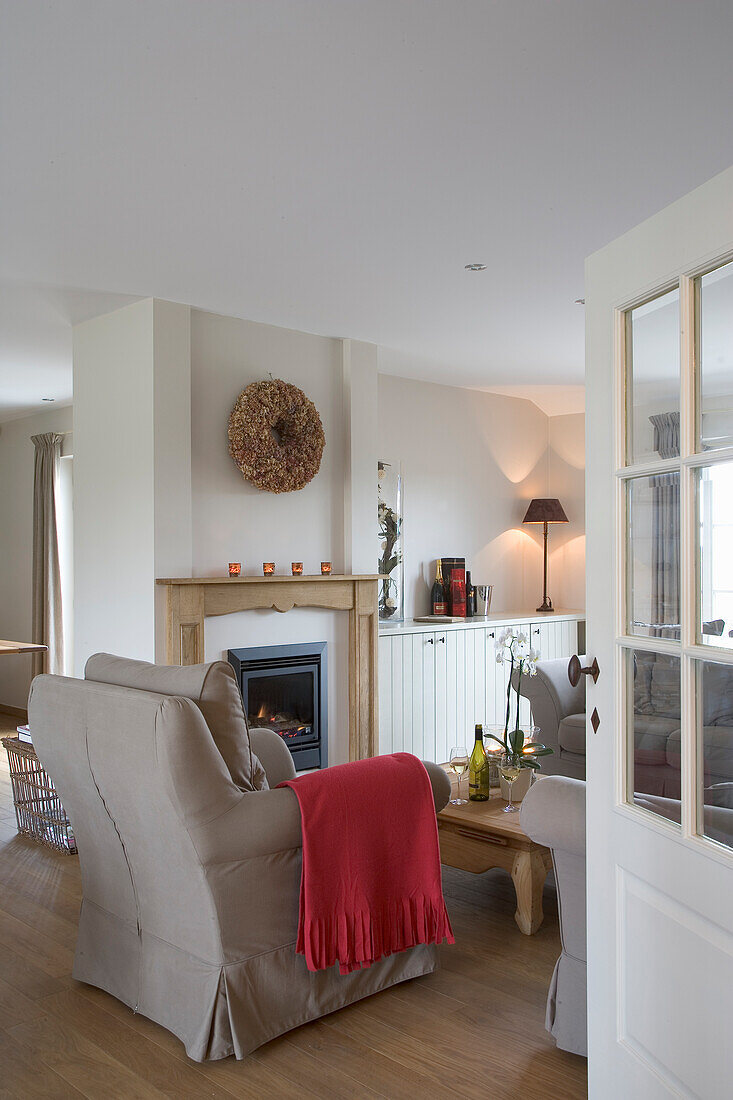 Living room with fireplace, beige armchair and red woollen blanket