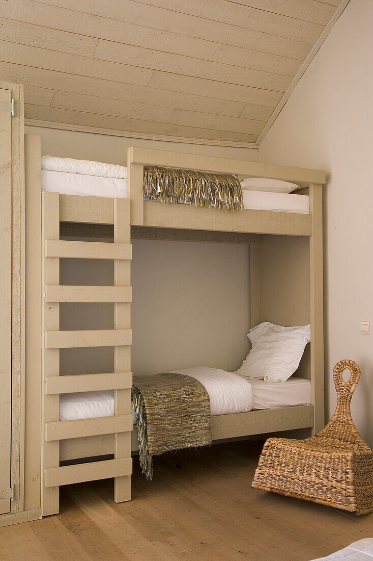 Bunk bed made of light-coloured wood in minimalist bedroom with wicker armchair