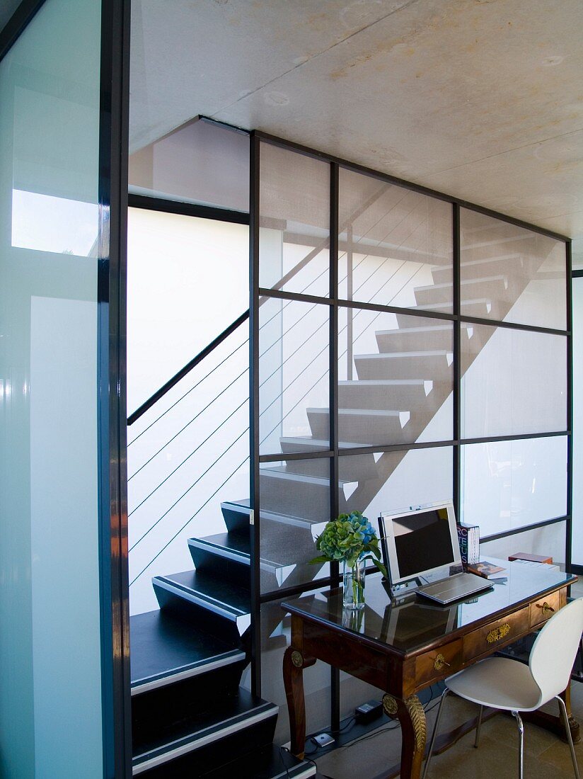 Anitker Schreibtisch mit weißem Schalenstuhl vor Treppenaufgang in zeitgenössischem Wohnhaus