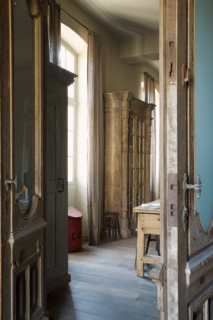 View of antique, rustic, glass-fronted cupboard though open interior doors in grand, old country house