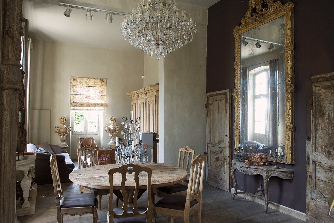 Mixture of styles in open-plan living-dining room with rustic wooden table and antique chairs opposite Rococo console table below gilt-framed mirror
