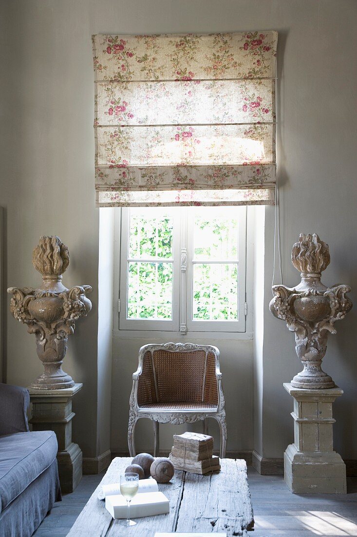 Stylised vases on plinths in antique Greek style and Rococo chair below window with half-closed Roman blind