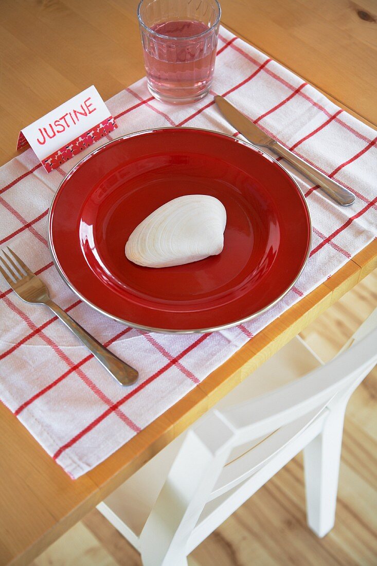Rustic place setting with red plate, seashell and place name