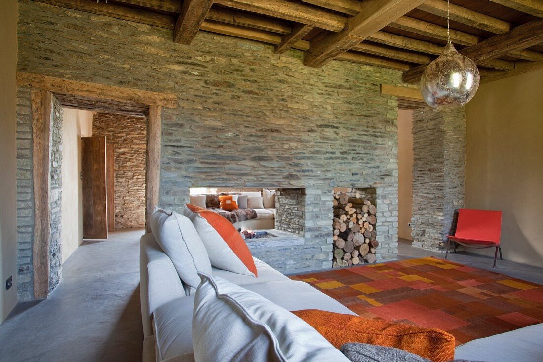Moderner Wohnraum mit rustikaler Holzbalkendecke und Kaminwand aus Naturstein als Raumteiler