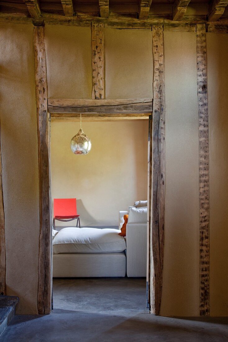 Durchgang in einer Fachwerkmauer mit Lehmausfachung - Blick auf ein helles modernes Sofa und von der Decke hängende Silberkugel