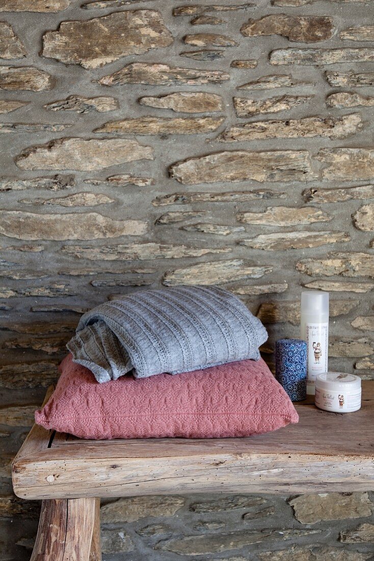 Cushions and toiletries on rough wooden bench against craggy stone wall