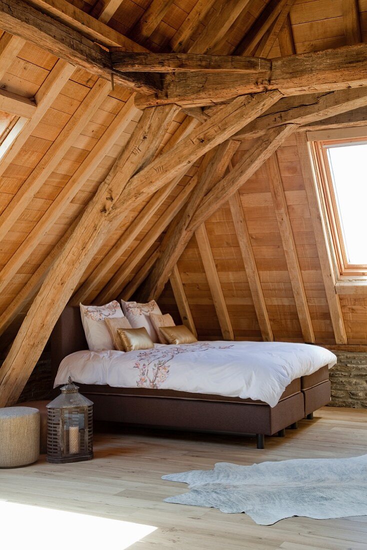 Double bed in attic under old roof structure with new wood-cladding and modern skylights