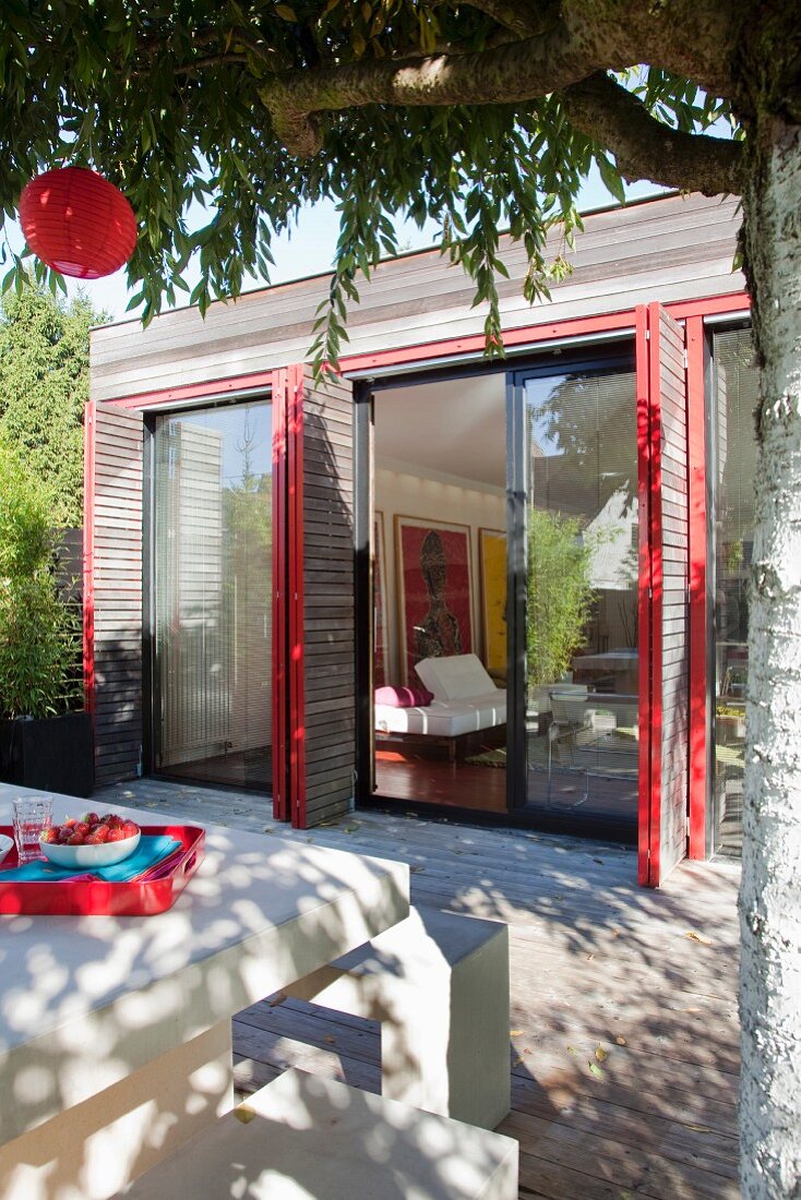 Weisser Terrassentisch mit Bank vor modernem Einfamilienhaus und klappbaren Fensterläden