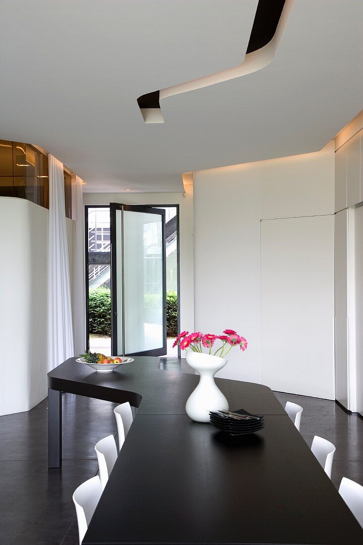 Gezackte Formen eines modernen, schwarzweissen Raumes, betont durch einen langen Esstisch und Lichtschlitze in der Decke