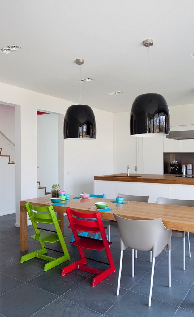 Roter und Grüner Kinderstuhl vor massiven Holztisch in offener Küche