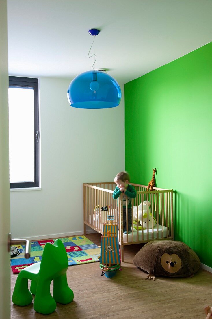 Green wall in nursery with cot and blue hemisphere lamp