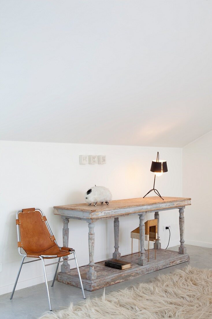 Modern chair with leather cover and console table in antique Greek style under sloping attic ceiling