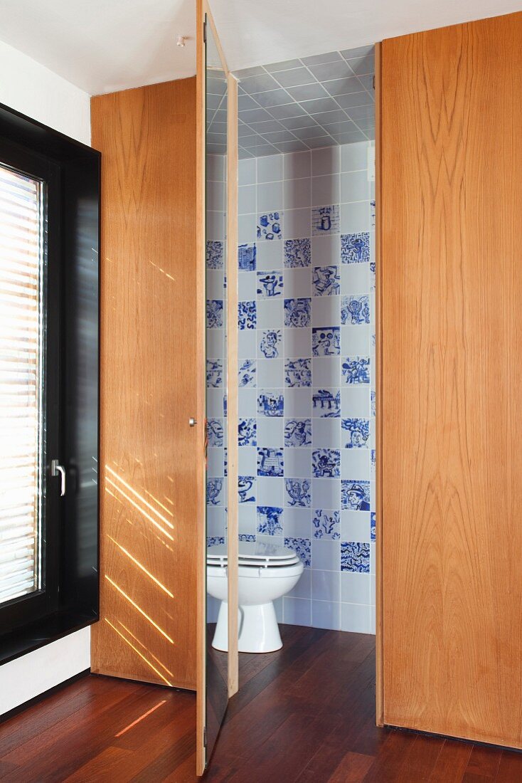 Wooden installation with open door and view into bathroom with toilet against tiled wall