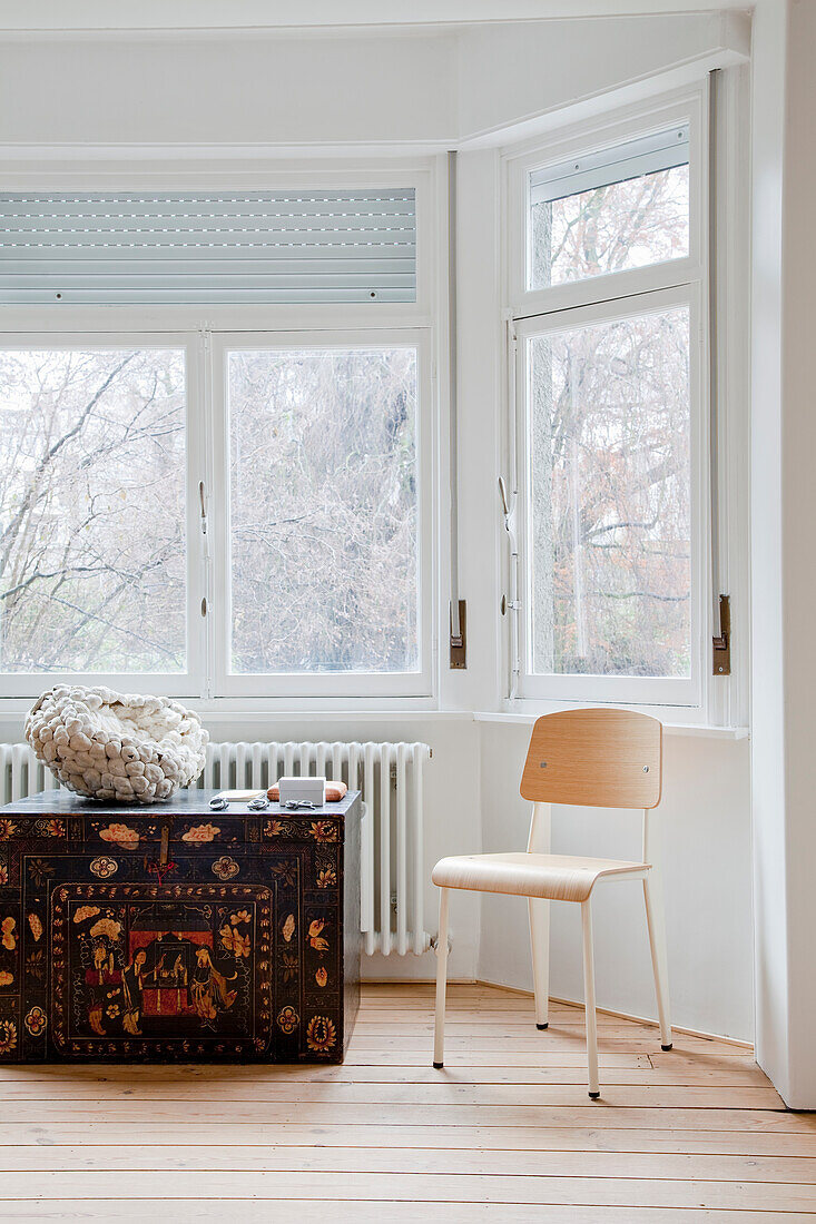 Bright room with antique chest, chair and window view of bare trees