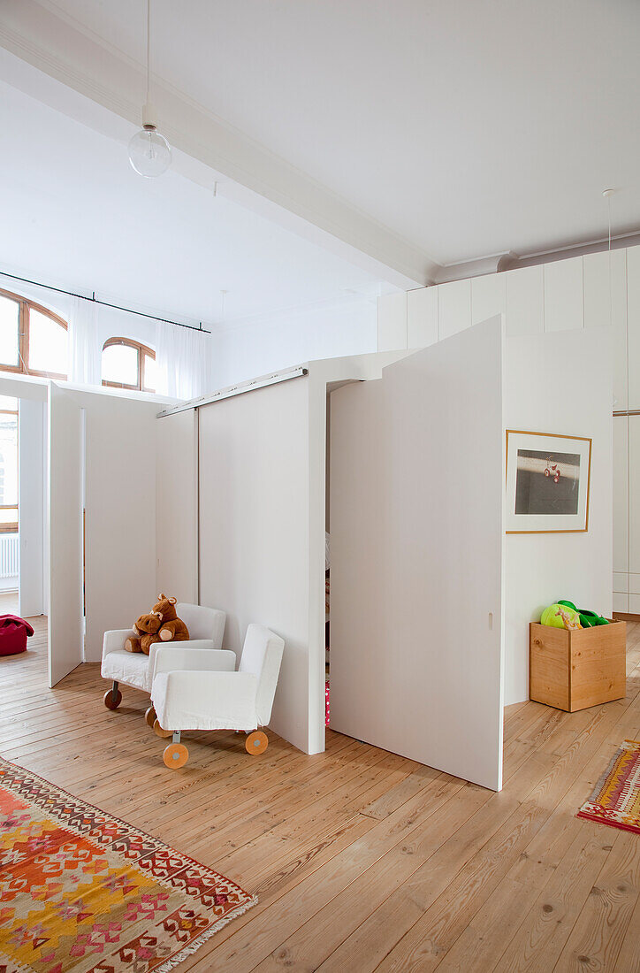 Brightly designed children's room with partitions and white armchairs on castors