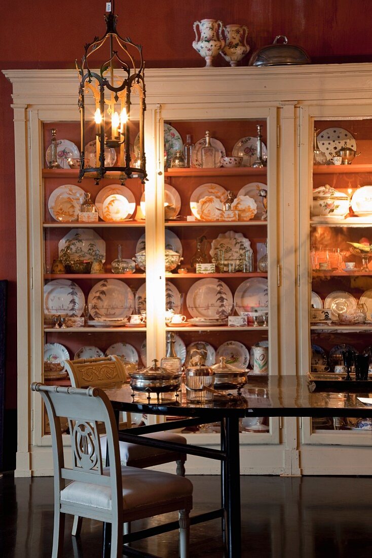 Antique dining room furniture in front of plate collection in display cabinet with soft illumination