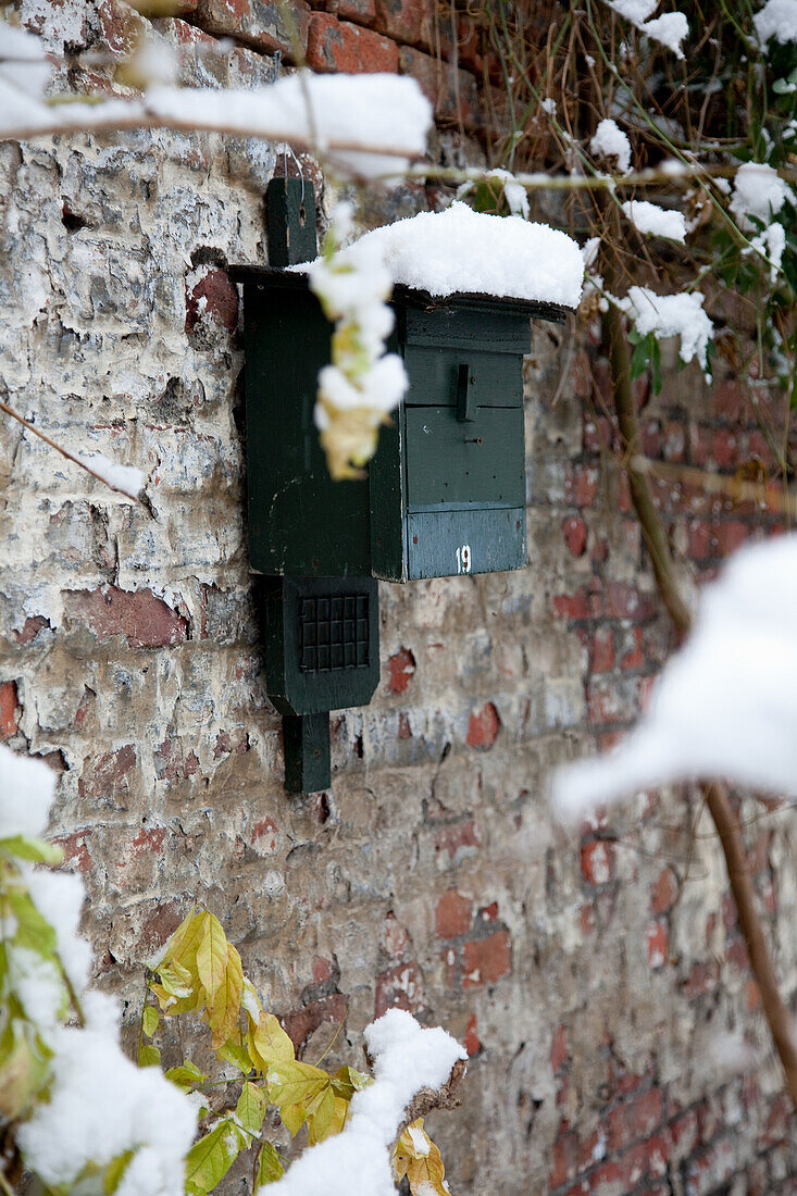 Snow-covered, green wooden letterbox on a brick wall