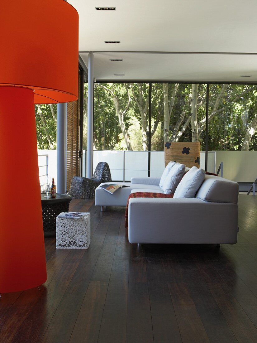 Weisses Sofa auf dunklem Parkettboden und orangefarbene Stehlampe in modernem Wohnraum