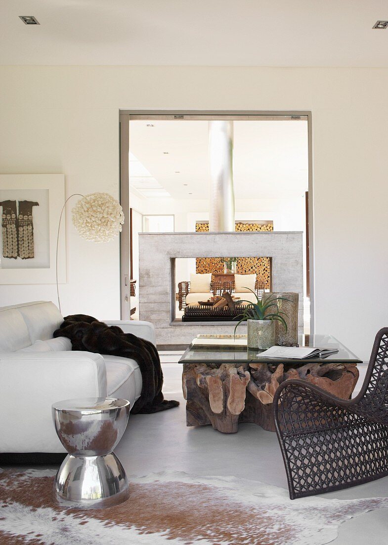 Wohnraum-Zimmerflucht mit freistehendem Kamin in Rahmenform / Glasplatte auf riesigem, verzweigtem Baumstamm und Edelstahl-Tischchen in Trommelform