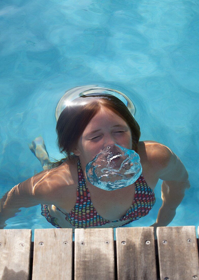 Pool with wooden walkway - girl in bikini blowing out large air bubbles underwater