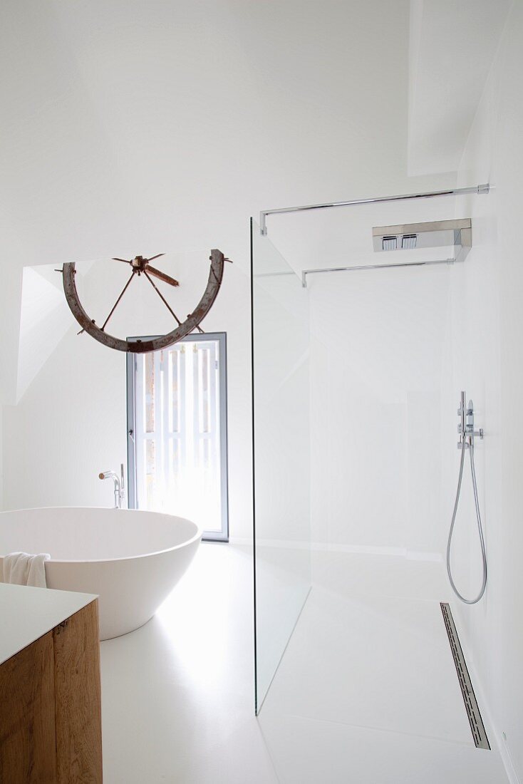 White bathroom with free-standing, round bathtub and open-plan wet area with glass partition