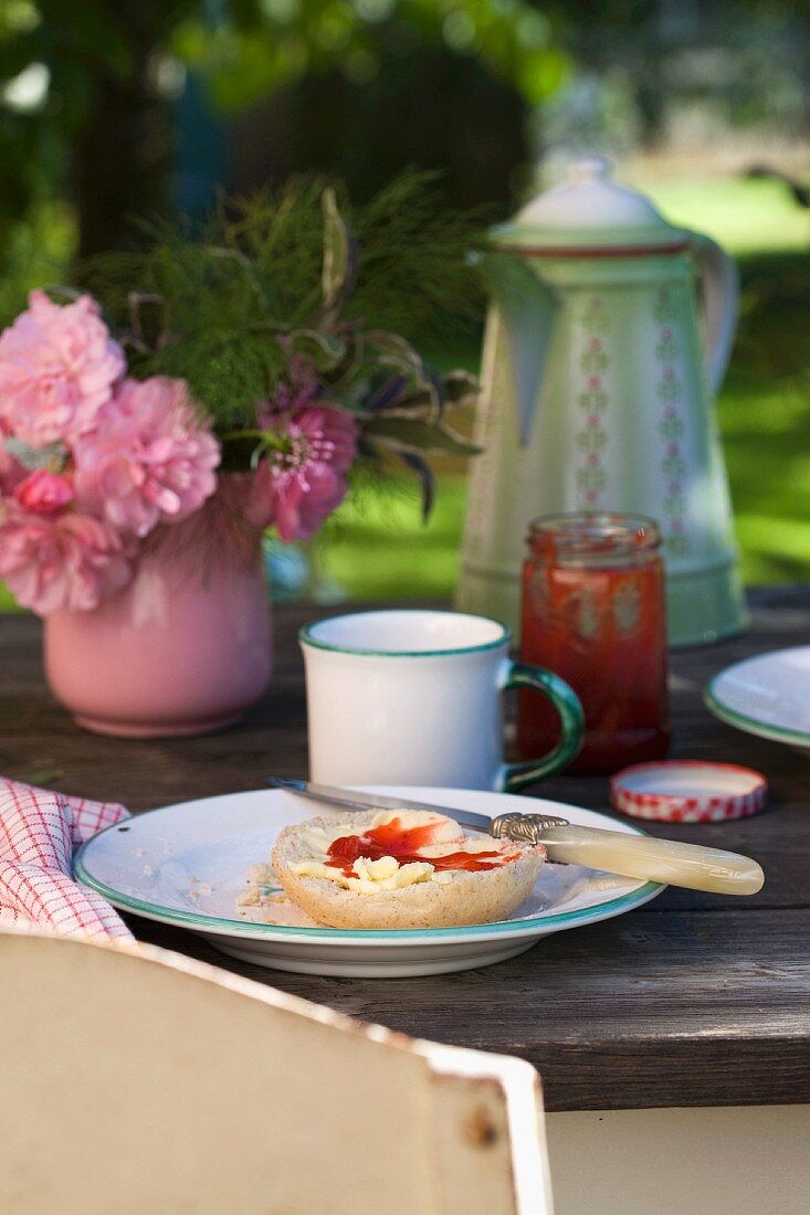 Rustikaler Holztisch mit Frühstücksbrötchen und kleinem Blumenstrauss im Garten
