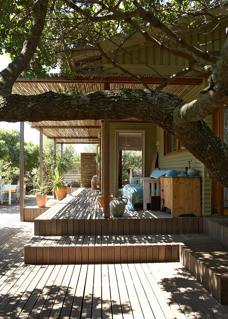 Holzterrasse mit Sitzmöbeln und Pflanzen vor einem Landhaus