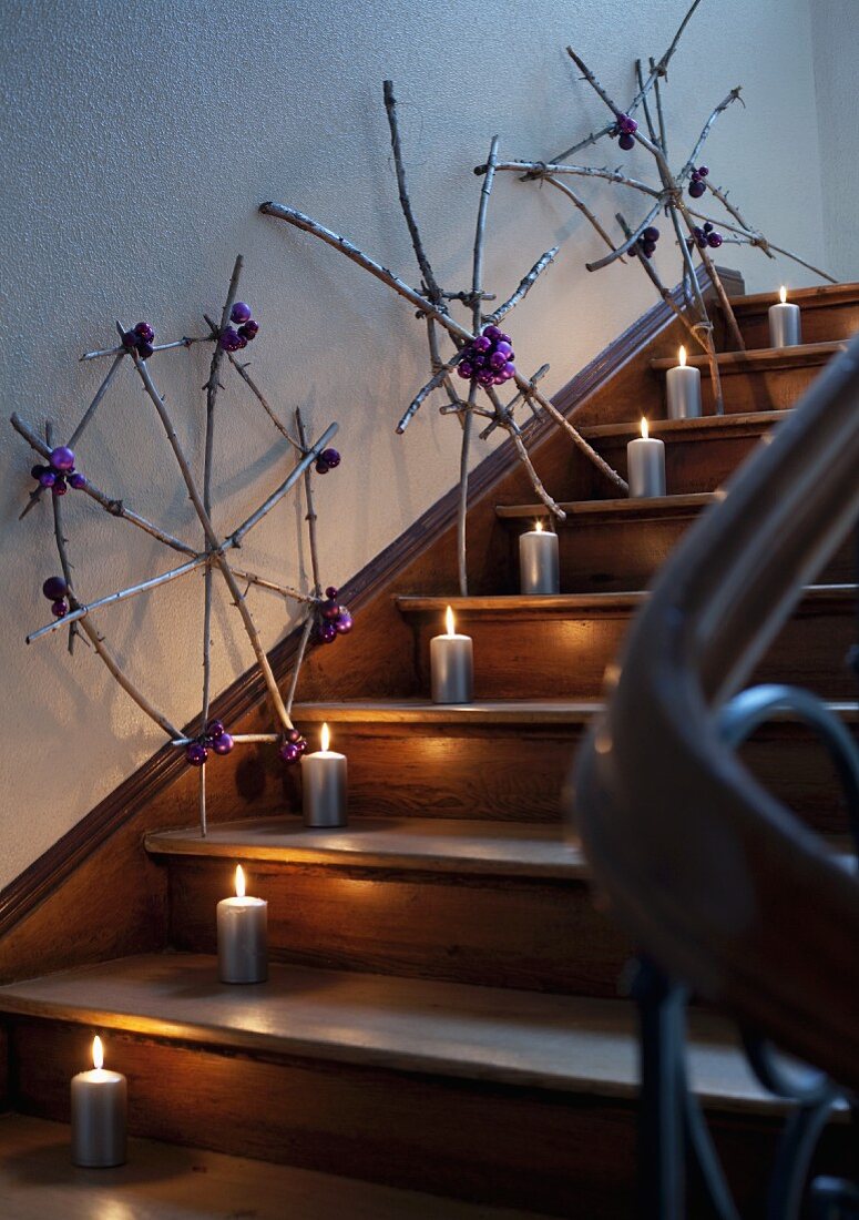 Sternformen aus zusammengebundenen Zweigen und Kerzen als Weihnachtsdekoration in einem Treppenhaus