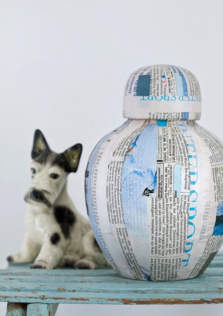 Originelle Vase aus Schreib- und Zeitungspapier mit Klarlack-Finish, daneben ein Porzellanhund