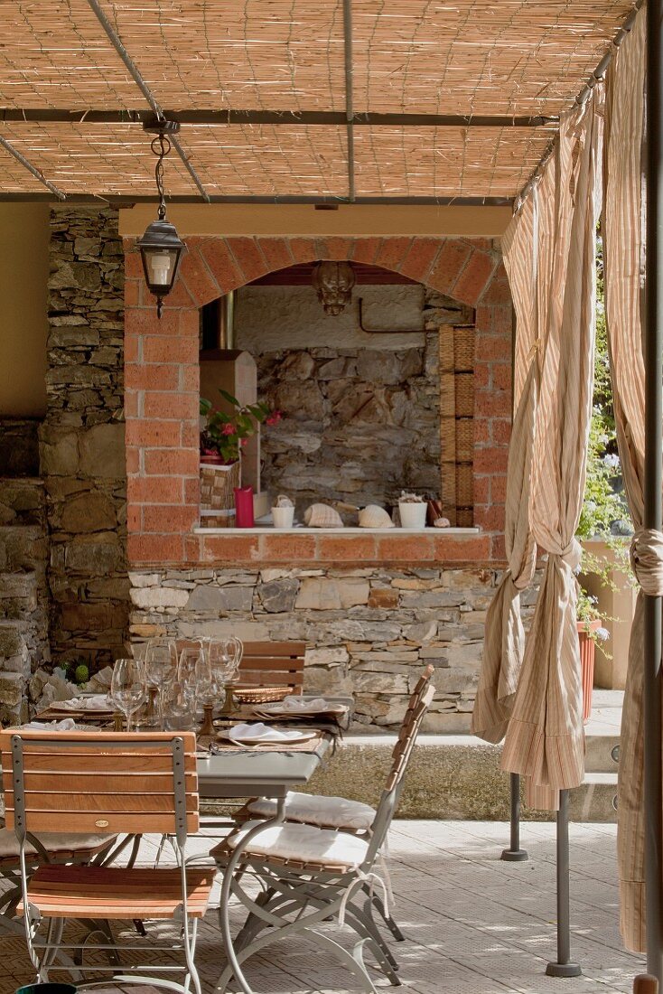 Terrasse in Naturfarben - gemauerte Kochecke und Retromöbel aus Metall unter Pergola in filigraner Stahlkonstruktion