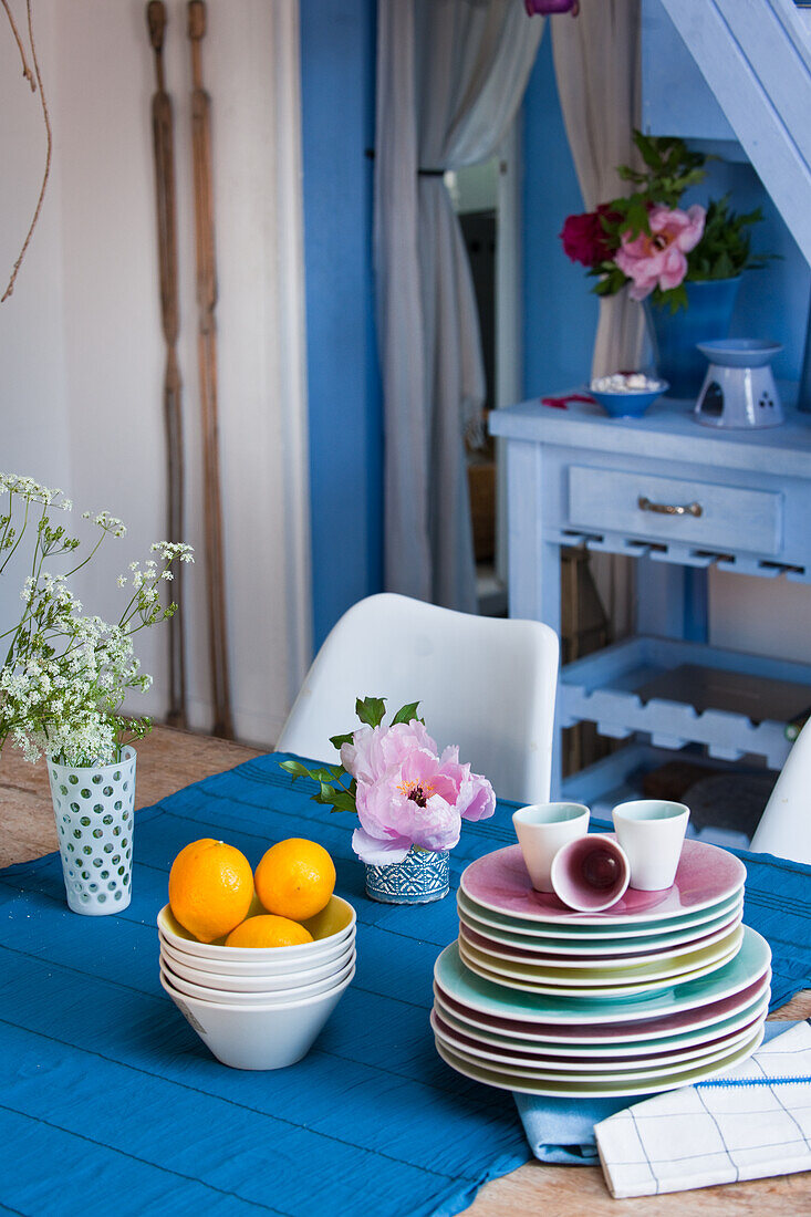 Geschirr und Blumenarrangement auf Holztisch mit blauem Tischläufer