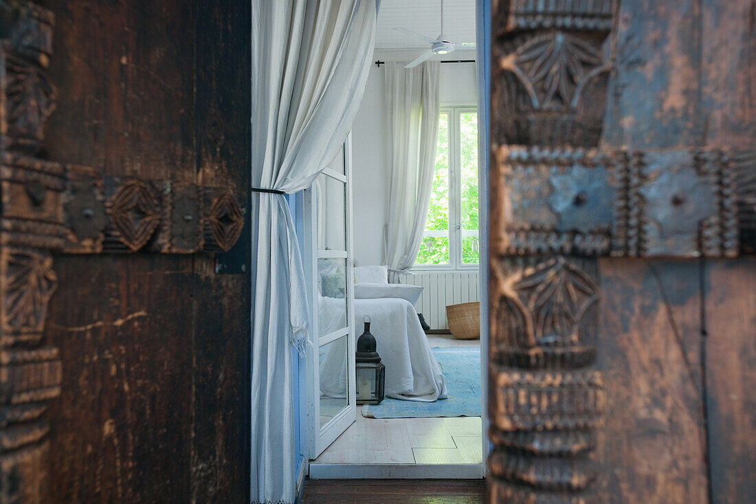 Offene geschnitzte Holztür, Blick in Zimmer mit weißen Wänden, weißem Boden und blauem Teppich