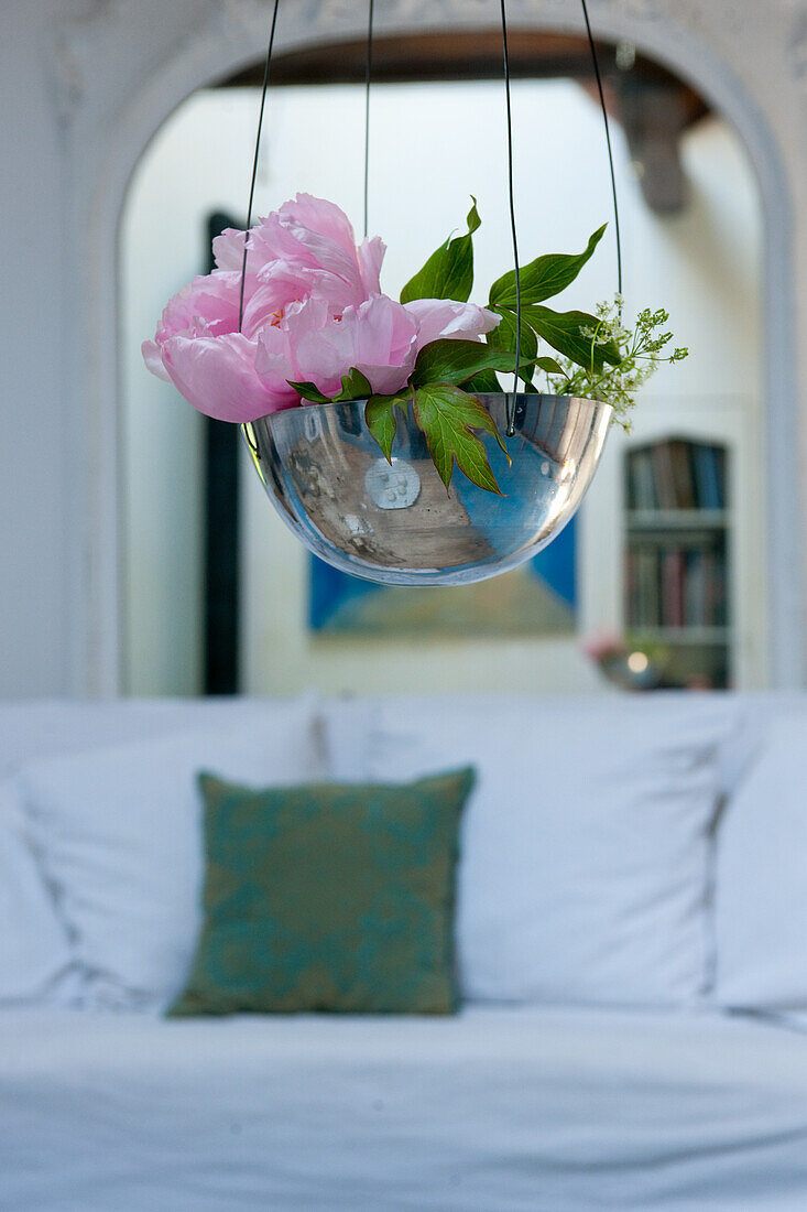 Hanging vase with peony (Paeonia) and greenery in front of white sofa