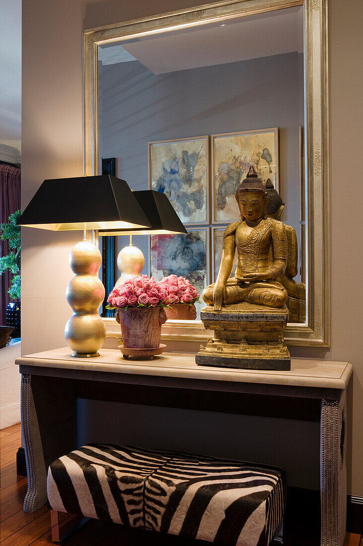 Console with golden Buddha statue and table lamp in front of wall mirror