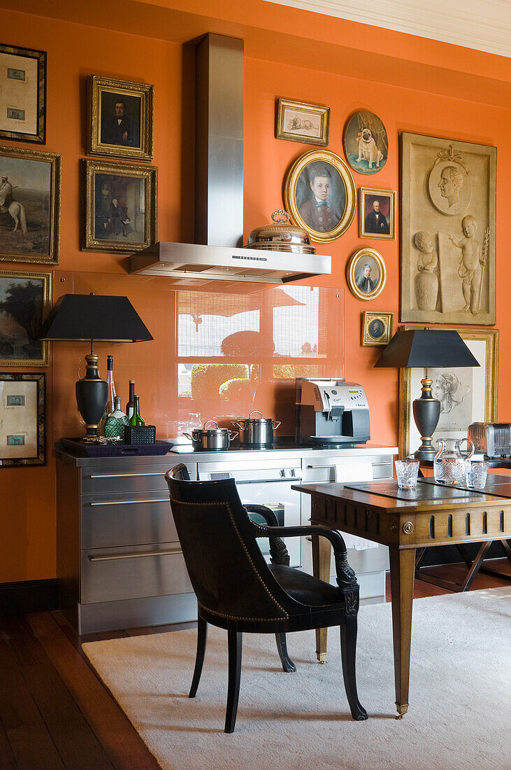 Small kitchen with stainless steel elements and orange-coloured wall with pictures