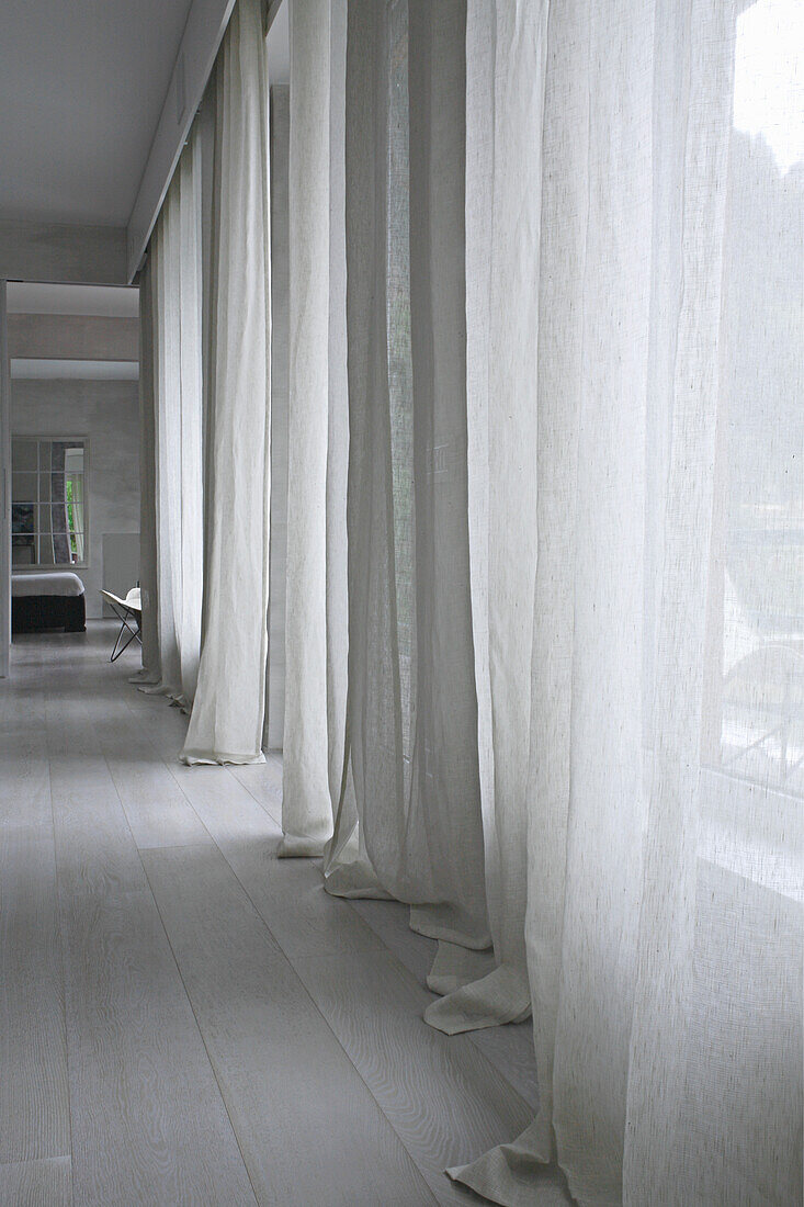 Bodenlange weiße Gardinen vor Fensterfront in hellem Raum