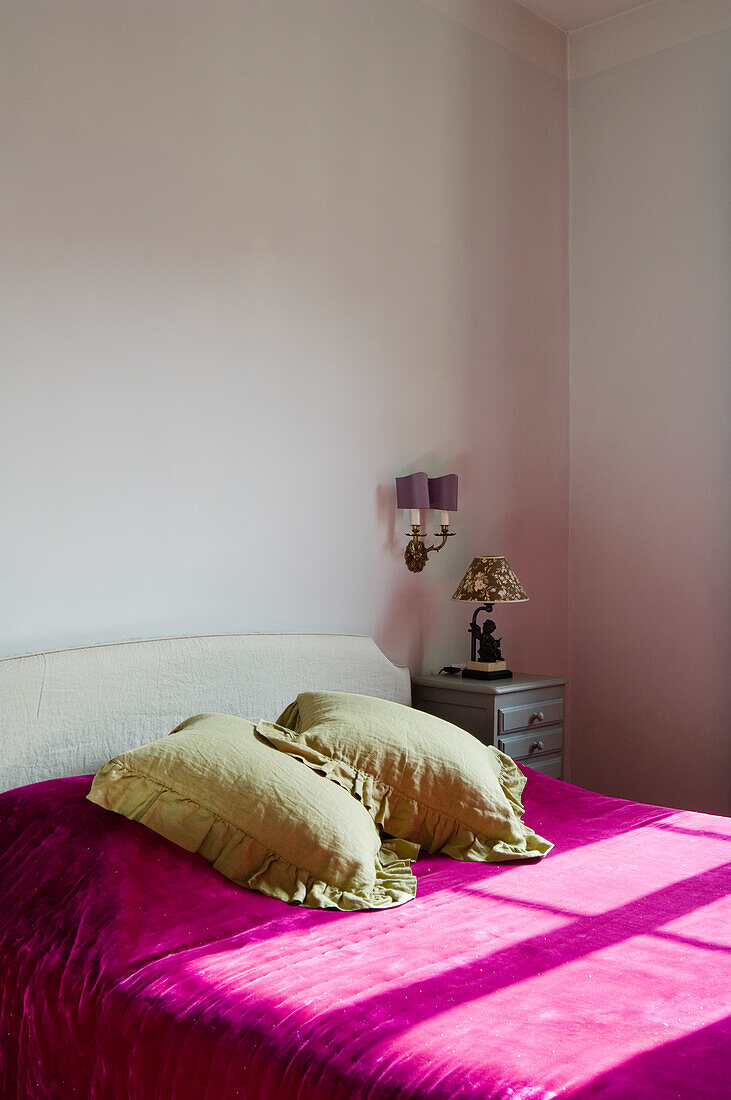 Schlafzimmer mit weißem Bett, pinker Tagesdecke und hellgrünen Kissen