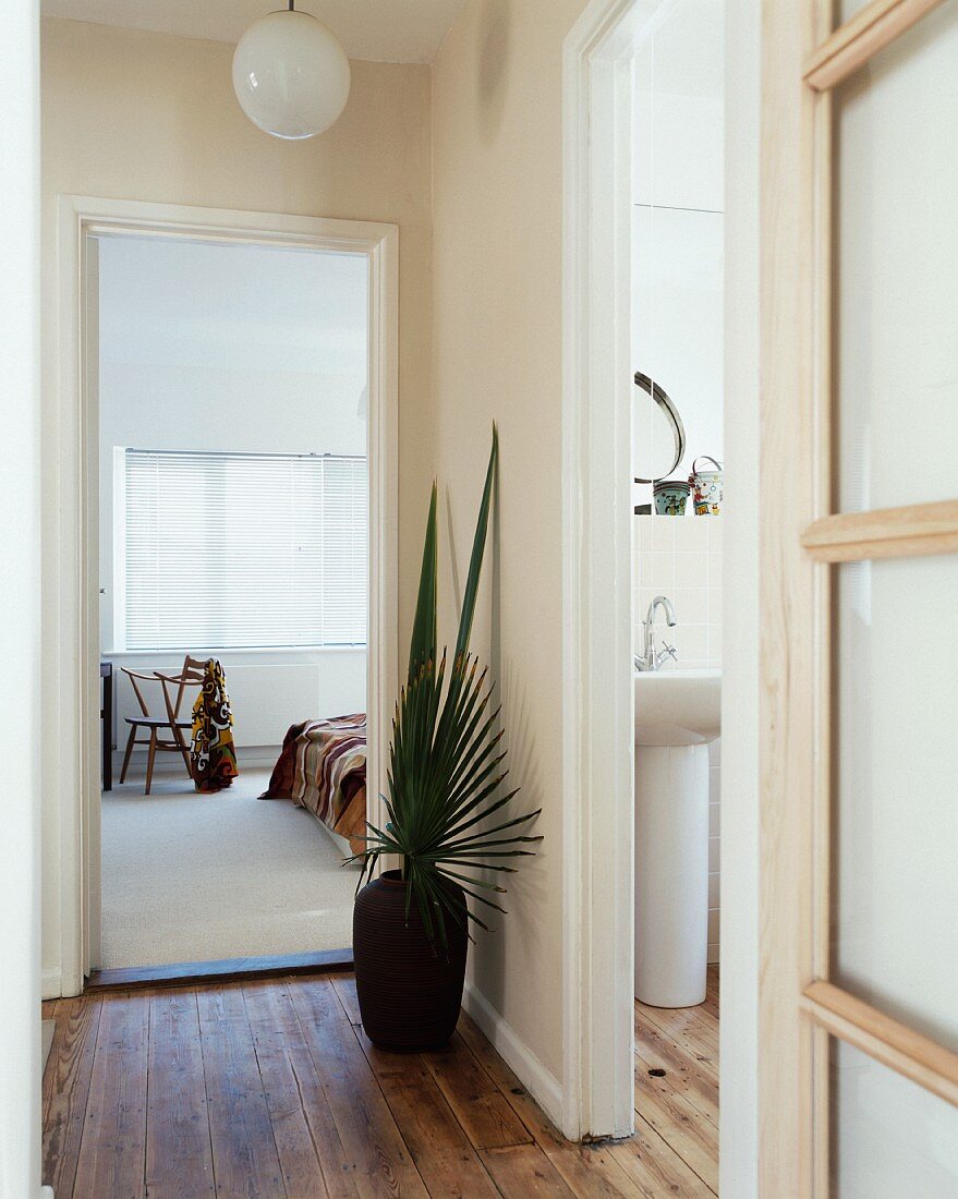 Bodenvase mit Palmenblättern im Flur neben offener Tür mit Blick ins Schlafzimmer