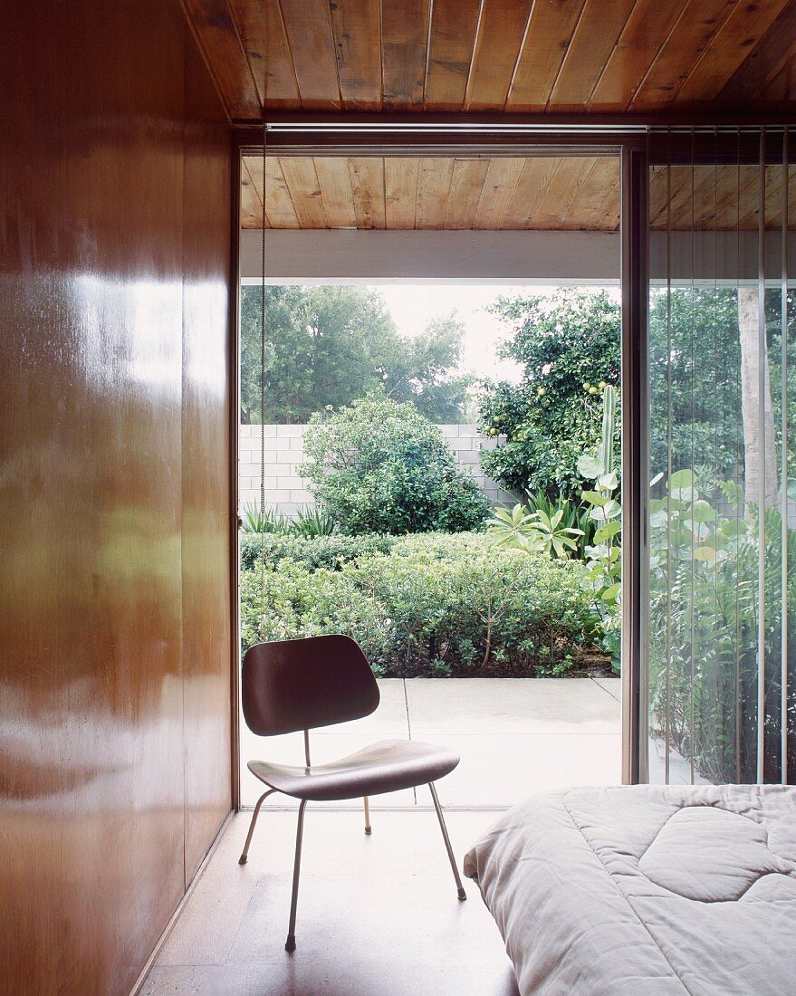 50s-style wooden chair in front of open terrace door in wood-panelled bedroom