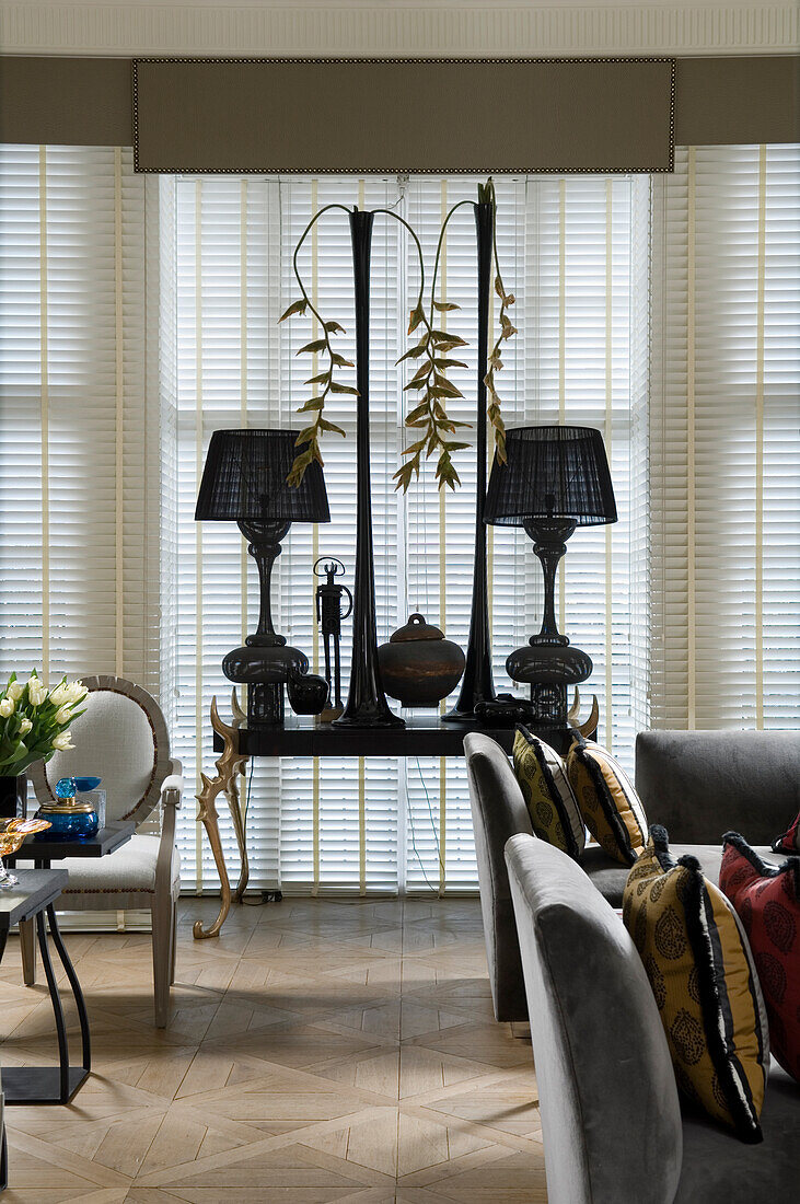 Console table in front of window with Roman blinds and table lamps