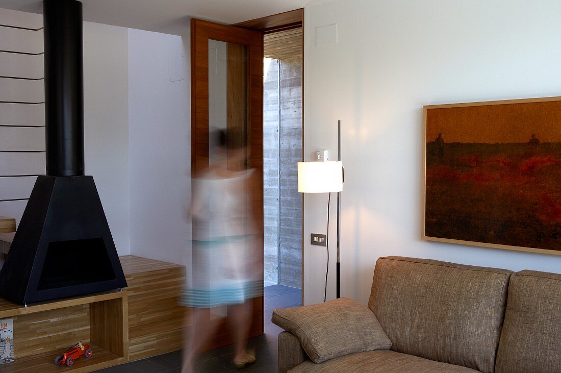 Ausschnitt eines Sofas mit Stehlampe, daneben verschwommen eine auf die Tür zugehende Frau