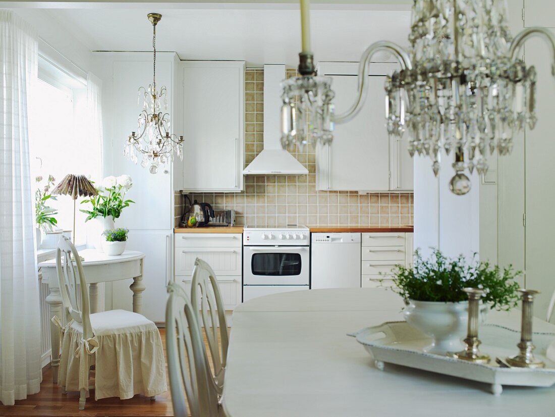Blick auf die Küchenzeile einer Wohnküche im klassisch-romantischen Stil mit weissen Vintage-Möbeln und Kronleuchtern