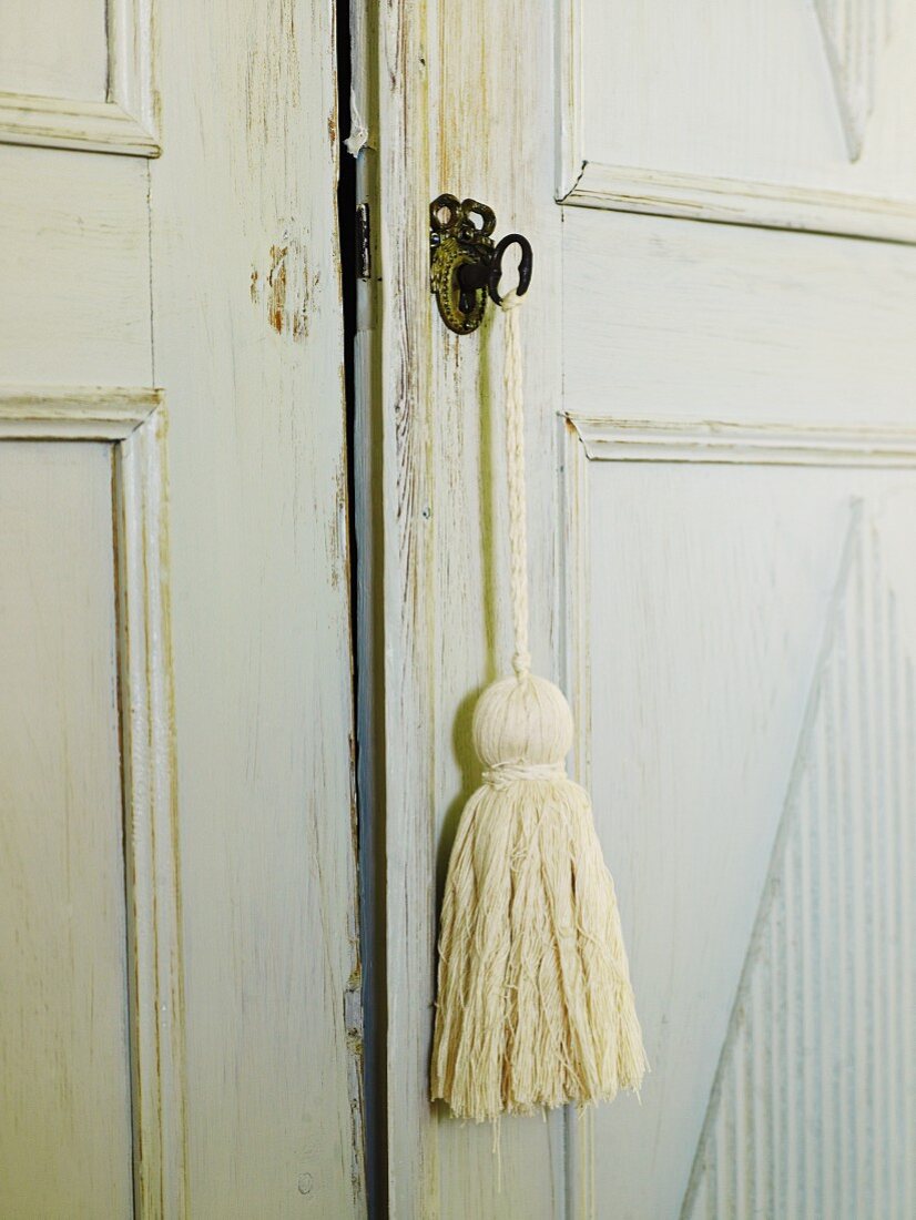 Detail of lock on shabby chic, antique cupboard with simple tassel hanging from key