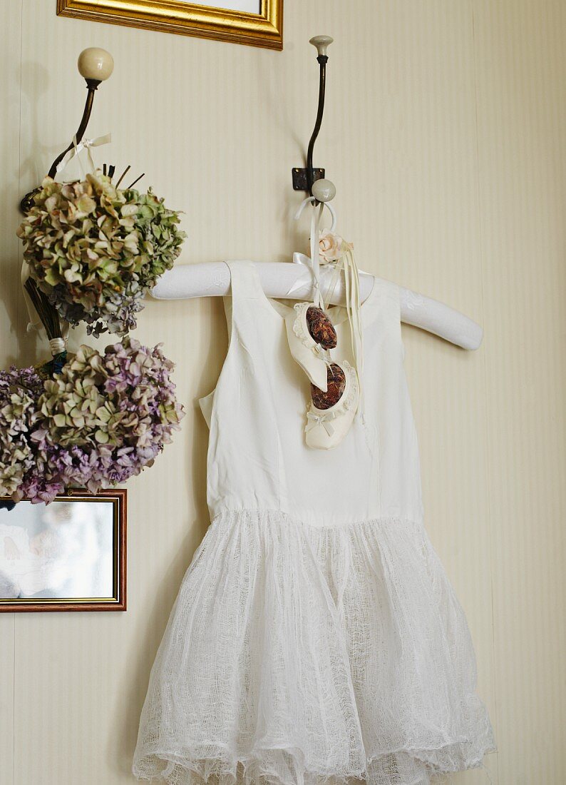 White baby's dress and shoes hanging from wall peg next to posies of dried flowers