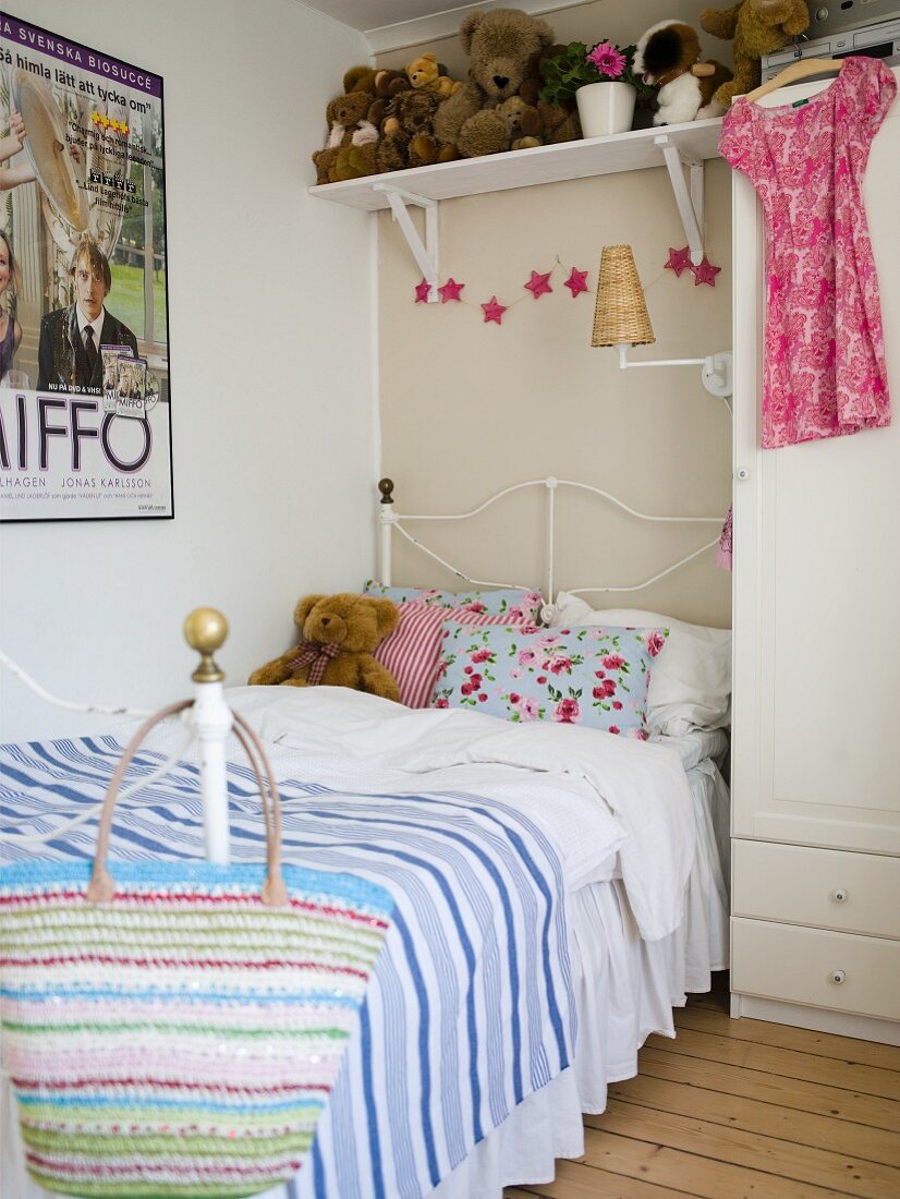 Girl's bedroom with iron bedstead below shelf of teddy bears