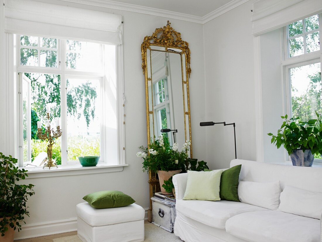 Wohnzimmer mit weißem Sofa, Zimmerpflanzen und Standspiegel mit Goldrahmen neben dem Fenster