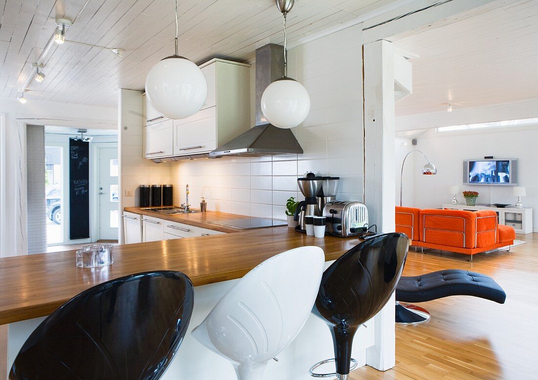 Schwarze und weiße Barhocker an der Küchentheke mit Blick in das Wohnzimmer